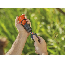 Une personne connecte un raccord Aquastop Gardena à un tuyau d''arrosage.
