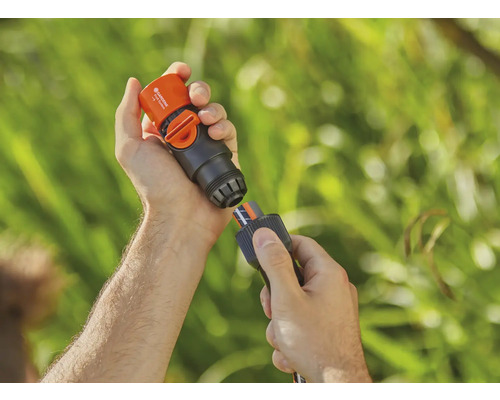 Une personne connecte un raccord Aquastop Gardena à un tuyau d''arrosage.