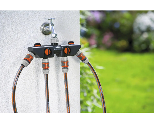 Gartenwasserhahn mit Gardena Verteiler und angeschlossenen Gartenschläuchen vor Garten