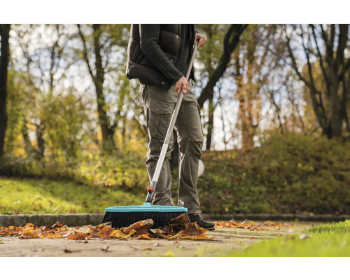 Eine Person kehrt Laub mit einem Strassenbesen im Aussenbereich.