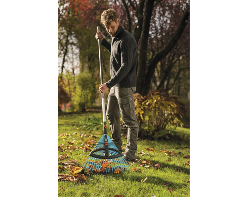 Ein Mann harkt Laub mit einem Laubbesen im Garten.