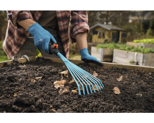 Une personne ratisse les feuilles mortes avec un râteau Gardena dans une plate-bande surélevée.