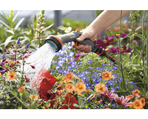 Eine Hand hält eine Gartenspritze und bewässert Blumen.