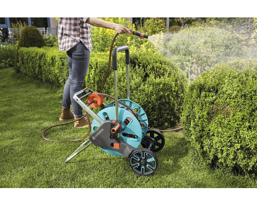 Femme arrose le jardin avec un chariot et un tuyau d''arrosage