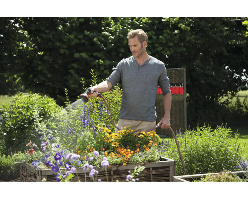 Un homme arrose des fleurs avec un tuyau d''arrosage dans le jardin.