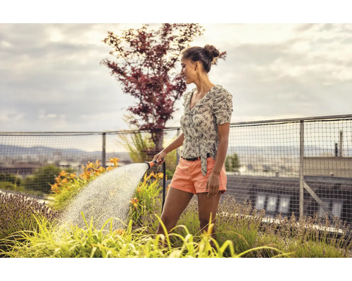 Frau giesst Pflanzen auf einem Dachgarten mit einem Gartenschlauch