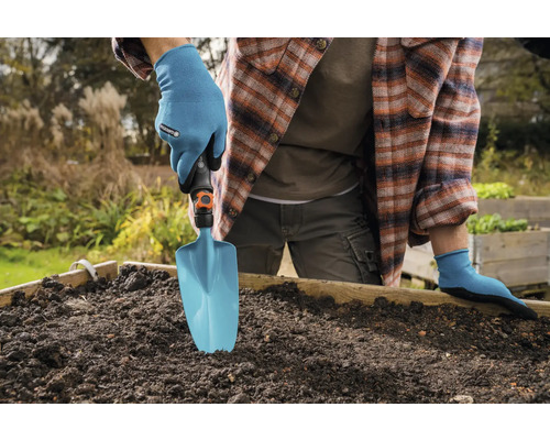 Person mit Gartenhandschuhen verwendet eine Gartenschaufel in einem Hochbeet.