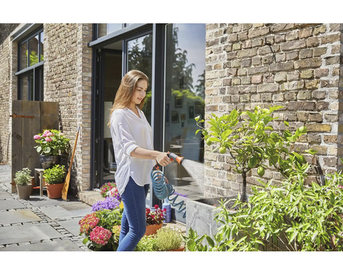 Une femme arrose des plantes avec un tuyau d''arrosage dans le jardin.