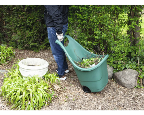 Une personne tire un chariot de jardin rempli de déchets de jardin dans un jardin