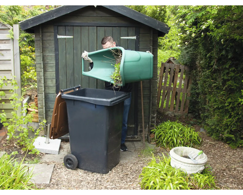 Un homme vide des déchets verts dans une poubelle de jardin