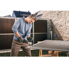 Un homme meule un portail métallique avec une meuleuse d'angle à l'extérieur.