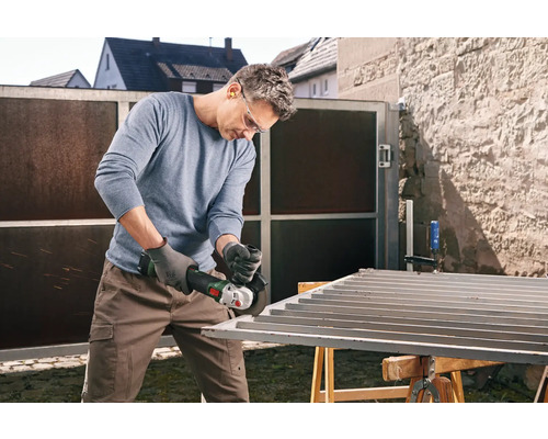 Un homme meule un portail métallique avec une meuleuse d'angle à l'extérieur.