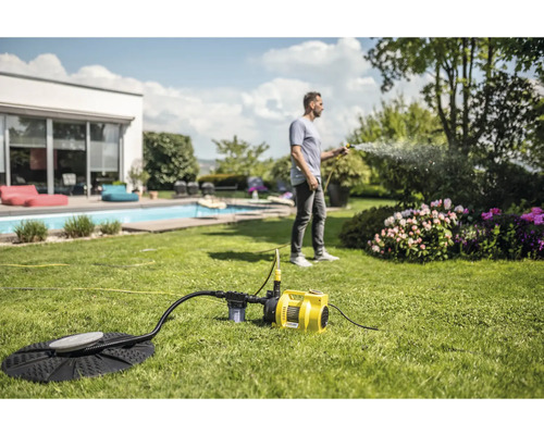 Un homme arrose des fleurs avec une pompe de jardin dans un jardin avec piscine.