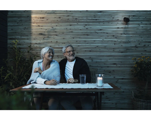 Älteres Paar sitzt bei Kerzenlicht an einem Tisch im Garten vor einer Holzwand