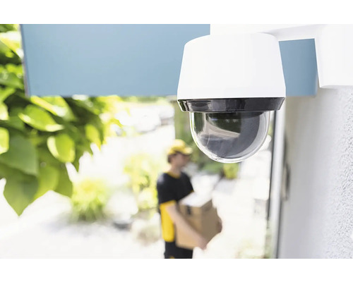 Überwachungskamera an einer Hauswand mit Paketbote im Hintergrund