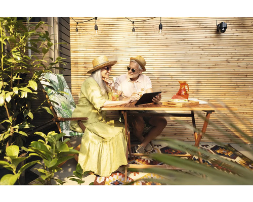 Ein Paar geniesst die Zeit im Garten mit einem Tablet am Holztisch.