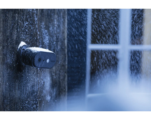 Eine Überwachungskamera ist bei Schneefall an einer Holzwand befestigt.