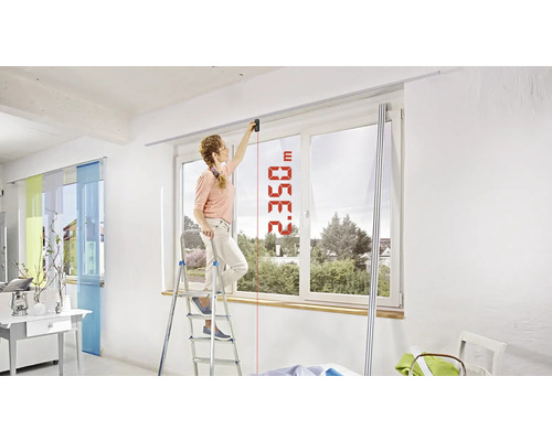 Frau misst Raumhöhe mit Laser-Entfernungsmesser auf Leiter