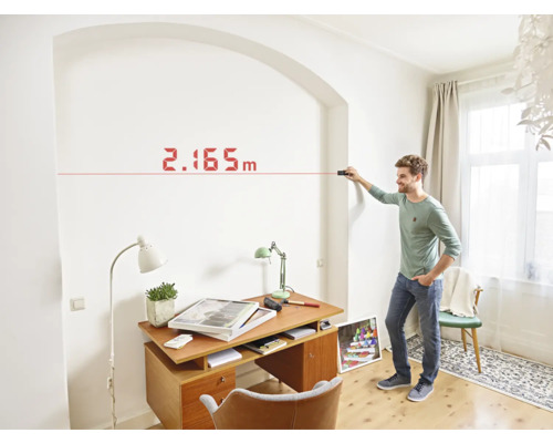 Mann misst eine Wand mit einem Laser-Entfernungsmesser in einem Zimmer.