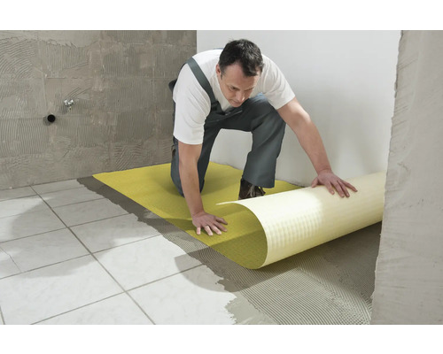 Un homme pose une natte de désolidarisation sur un sol carrelé.