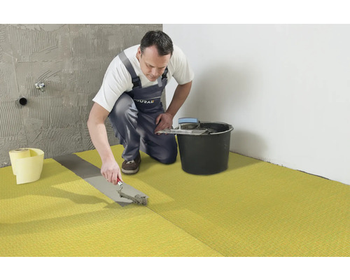 Un artisan pose une natte de désolidarisation dans une salle de bains.