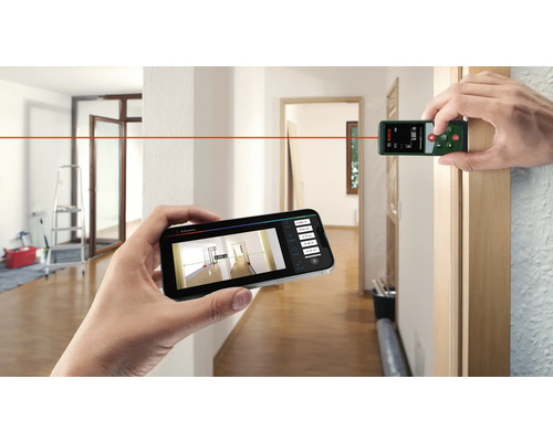 Person misst Raum mit Laser-Entfernungsmesser und Smartphone in hellem Flur