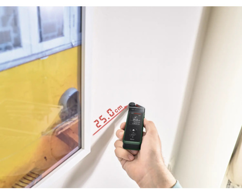 Eine Person misst mit einem Laser-Entfernungsmesser den Abstand an einer Wand.