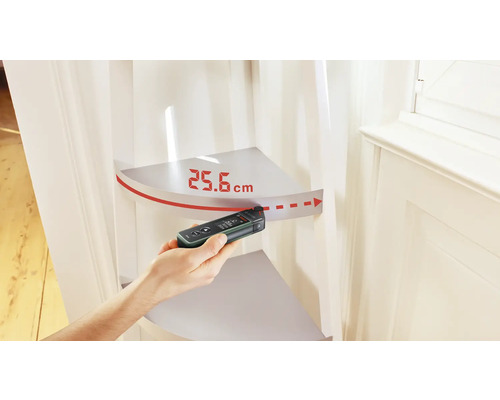 Eine Hand misst mit einem digitalen Entfernungsmesser 25,6 Zentimeter.