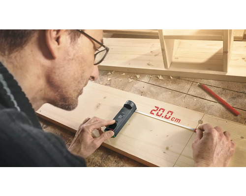 Handwerker misst ein Holzbrett mit einem digitalen Entfernungsmesser.