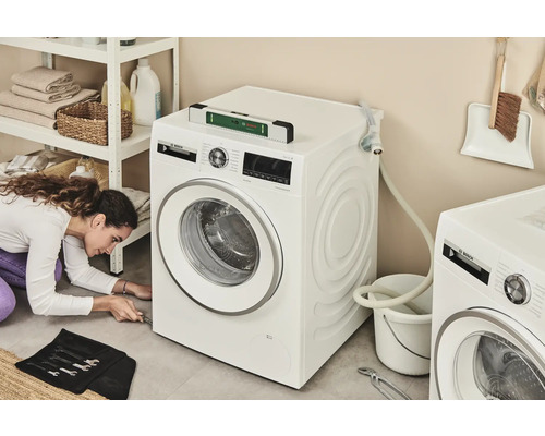 Frau repariert Waschmaschine im Waschraum mit Werkzeug