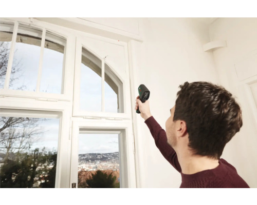 Mann misst Temperatur am Fenster mit Thermometer