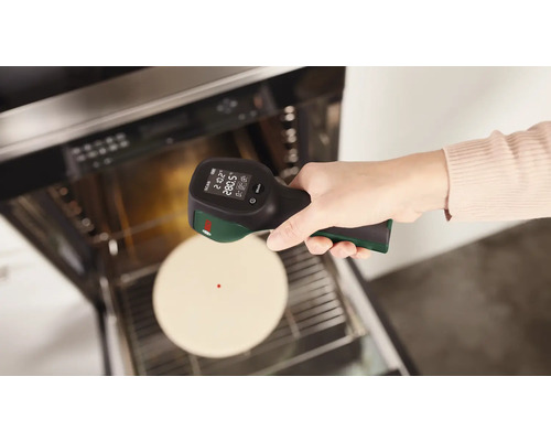Eine Hand hält ein Infrarot-Thermometer auf einen Ofen mit Speisen.