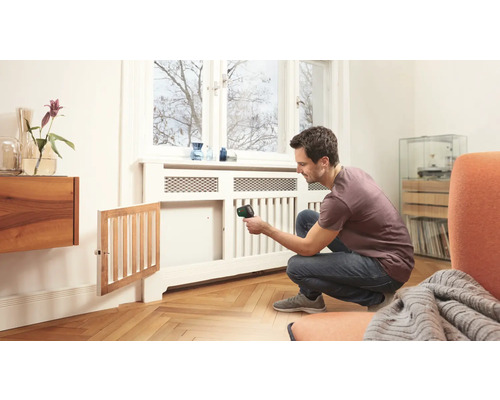 Ein Mann benutzt ein Thermometer, um die Temperatur eines Heizkörpers im Innenbereich zu messen.