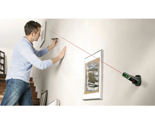 Un homme aligne des tableaux au mur à l''aide d''un laser à lignes croisées