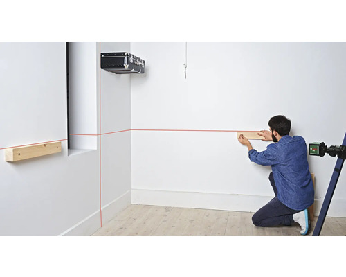 Mann befestigt mit einem Laser und Holzlatten eine Holzkonstruktion an einer Wand.