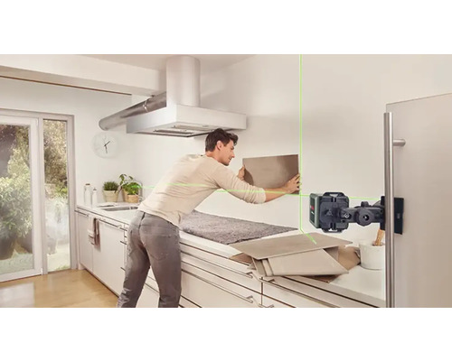 Mann befestigt Fliesen mit einem Linienlaser in einer Küche