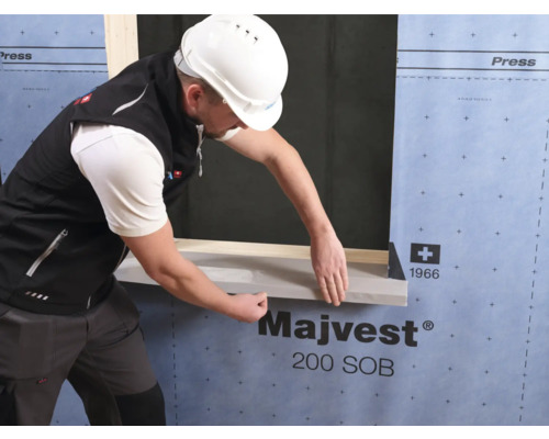 Un ouvrier du bâtiment pose un joint sur une ouverture de fenêtre. La façade est recouverte d''une membrane.