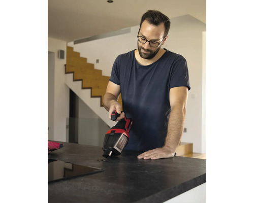 Ein Mann benutzt einen Akku-Handsauger auf einer Küchentheke, um Schmutz zu entfernen.