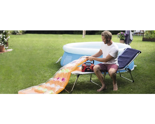 Un homme gonfle un matelas pneumatique avec une pompe à air dans le jardin, une piscine en arrière-plan