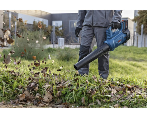 Une personne utilise un souffleur de feuilles sans fil Bosch dans le jardin pour enlever les feuilles.