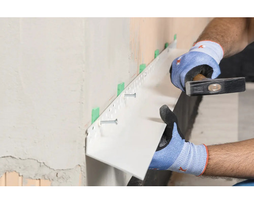 Handwerker befestigt Sockelprofil mit Hammer an Wand