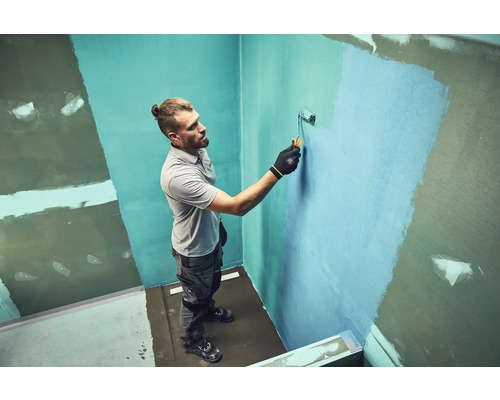 Un homme peint un mur avec un rouleau à peinture dans une salle de bain