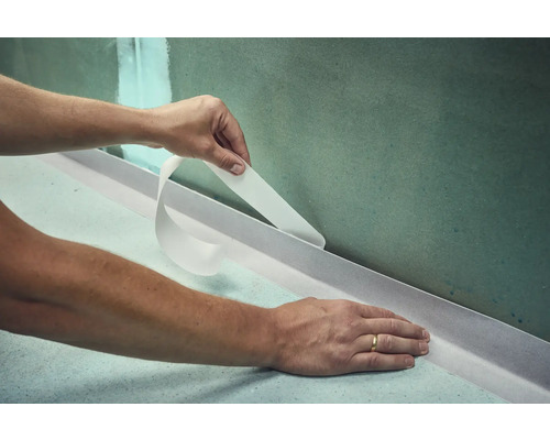 Application de bande d''étanchéité dans la salle de bains pour sceller le mur et le sol.