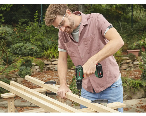 Un homme perce une planche de bois avec une perceuse sans fil dans le jardin.