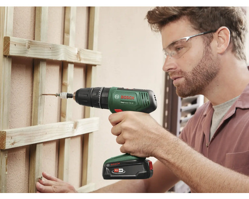 Un homme visse une vis avec une visseuse sans fil dans une construction en bois