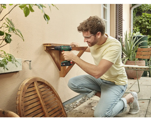 Un homme fixe une table en bois à un mur extérieur à l'aide d'une visseuse sans fil.