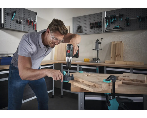 Mann bohrt mit einer Bohrmaschine Dübellöcher in ein Holzbrett auf einer Werkbank.