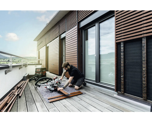 Un homme travaille avec une scie à onglet sur un balcon pour travailler le bois. Un aspirateur est prêt.