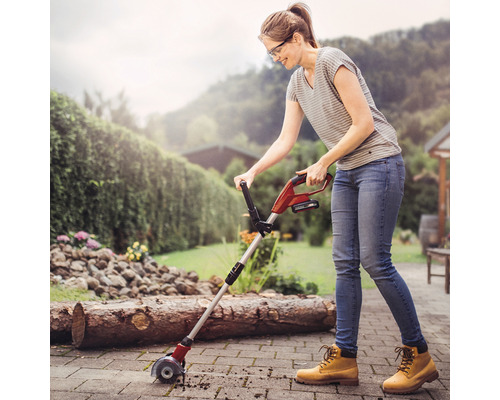 Une femme travaille avec une brosse à joints à batterie sur une surface pavée dans le jardin.