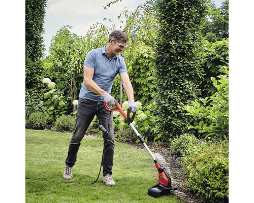 Un homme utilise un coupe-bordures dans un jardin.
